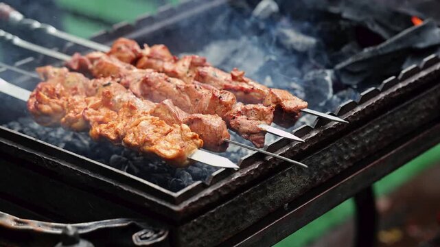 Meat skewers grilling on charcoal barbecue. Shashlik roasting over hot coals with smoke. Outdoor picnic and street food cooking concept. Traditional barbecue preparation.