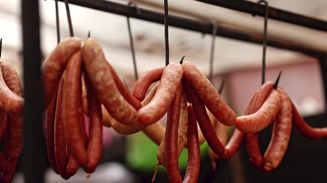 Traditional sausages hanging on hooks at street food market. Smoked meat products drying on rack. Delicious fresh sausage for sale at farmers market stall