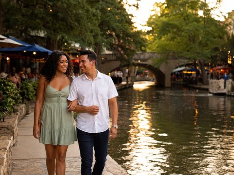 Gl&uuml;ckliches Paar spaziert bei warmem Abendlicht entlang des River Walk in San Antonio. Die romantische Stadtreise zeigt lokalen Tourismus, Restaurants und texanische Lebensfreude.