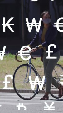 Animation of global currency symbols over asian woman in face mask wheeling bike in street