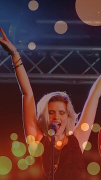 Animation of glowing spots falling over caucasian female singer holding a guitar singing at concert