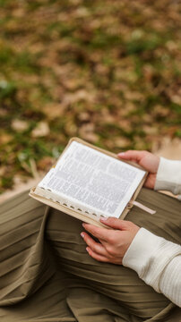 Woman in a pleated skirt reading a book outdoors on a grassy background