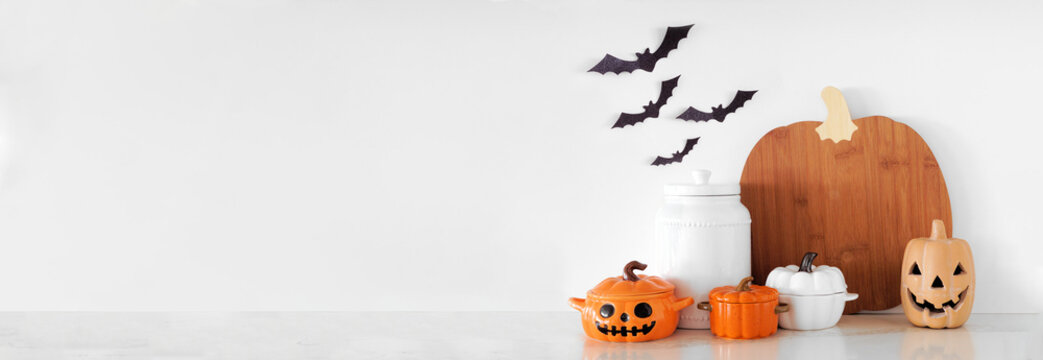 Halloween pumpkin theme kitchenware on a white stone countertop. Banner against a white wall background with copy space. Autumn kitchen decor concept.