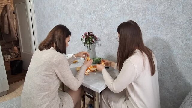 Two women preparing and enjoying food at a small table in a cozy indoor space