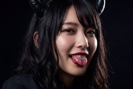 悪魔の角をつけて舌を出すイタズラな笑顔の若い女性のポートレート
