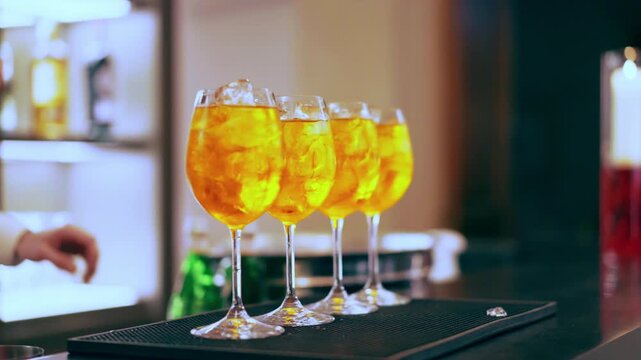 Glasses with Aperol Spritz cocktails at the bar counter, bartender preparing refreshing drinks for serving aperitif party celebration
