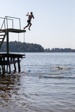 Man jumping into lake water from high diving board tower during summer, outdoor swimming and active leisure background. Active lifestyle photo