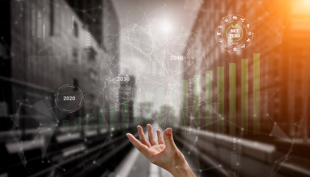 A hand reaches towards a futuristic digital display of graphs representing sustainable growth and net zero targets for 2020, 2030, and 2040 in an urban environment. Gantry