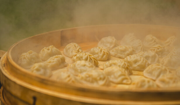 Steamed dumplings cooking in bamboo steamer with rising steam. Traditional asian food preparation, dumplings in steamer basket. Street food cuisine concept
