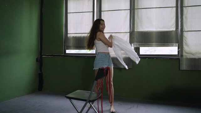 Happy and psychopathic Asian woman with unusual mental health issues is dancing alone pretending to be happy with red rope and chair in her room. Lonely female is stressed and about a failed life. 