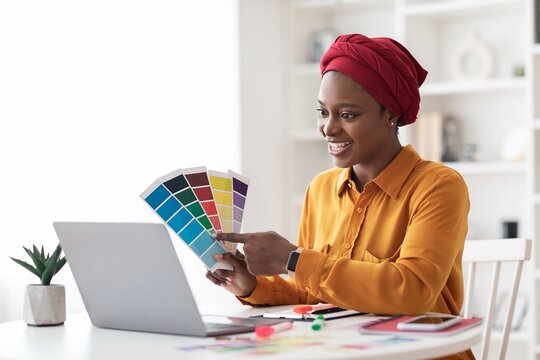 Smiling Black Woman Engaged In Choosing Color Palette For Interior Design While Sitting At Home Office. Happy Female Professional Working On Creative Project In Modern Workspace. Business Concept.