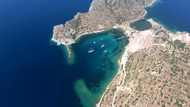 Yachts rest in a turquoise bay at Knidos, Datca, where rocky shores frame clear coastal water. Anchored sailboats and sheltered cove create a tranquil Aegean scene with charter travel appeal.