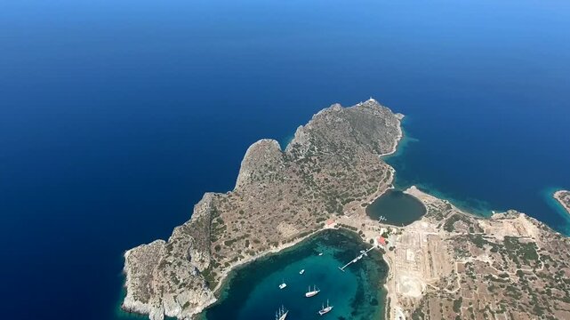 Yachts rest in a turquoise bay at Knidos, Datca, where rocky shores frame clear coastal water. Anchored sailboats and sheltered cove create a tranquil Aegean scene with charter travel appeal.