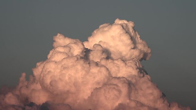 Sunset timelapse captures swelling foamy cumulus cloud rising across dramatic sky. Evening atmosphere shows billowing white cloud mass expanding through golden dusk light.