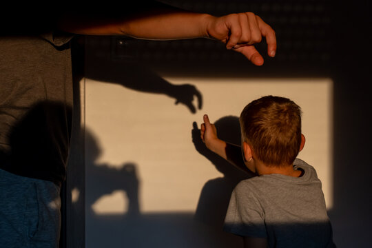 Children creating animal shadow puppets with their hands on a sunlit wall at home. Concept of imaginative play, sibling cooperation, screen-free entertainment and creative childhood development.