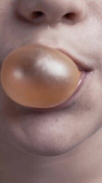 Boy chews gum and blows a large translucent bubble. Extreme close-up of mouth, lips and tongue. Playful childhood moment.