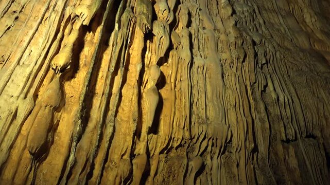 Limestone stalactites hang inside a cave, showing karst formations and underground texture. Dripstone structure and lit chamber create a subterranean scene with natural detail.