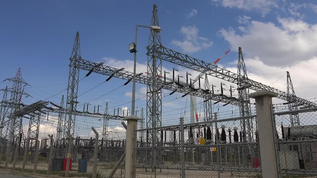 Wind energy power plant sends electric current to industrial transformer switchyard. Renewable turbine infrastructure channels electricity through grid substation equipment.