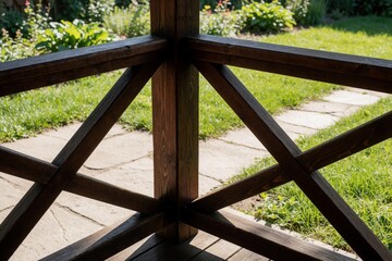 Obraz premium Wooden porch railing detail overlooks a sunlit garden path. Dark brown wood structure frames rich green grass and plants. Outdoor relaxation space in summer.