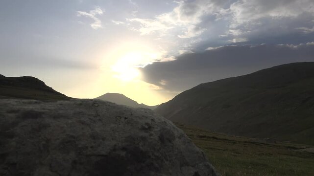 Sunrise lights a rugged mountain valley, warming barren hills and treeless highland slopes. Daybreak sky and golden light reveal rocky terrain, open ridges, and expansive alpine scenery.