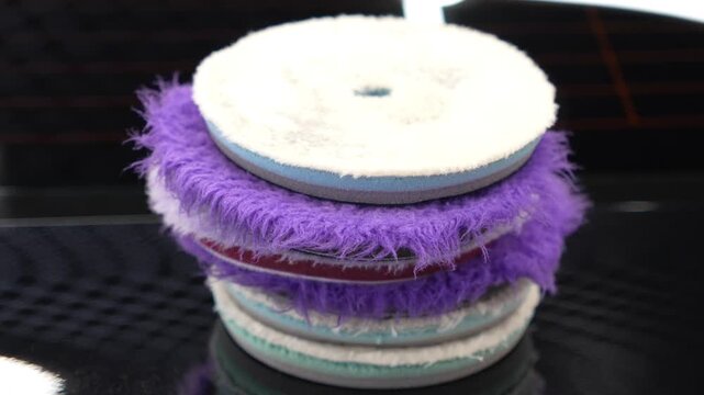Close up of a stack of professional car detailing buffing pads. Multicolored wool and microfiber polishing wheels for electric dual action orbital machines in a garage auto workshop service station.