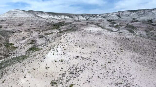 Aerial view shows eroded mesa hills with white limestone layers across barren arid ground. Wind and rain sculpt pale strata into striking geological relief and desert landforms.