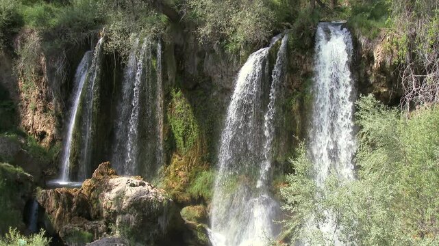 Sizir Waterfall in Sivas Turkey cascades through green valley and bright river stones in sun. Fixed camera records sparkling flow rocky channel calm Anatolian nature scene beneath vivid weather.