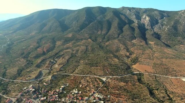 Aerial view of hillside village in western Turkey, Aegean region, Mugla Datca countryside. Forest slopes and orchards surround rural homes above coastal Mediterranean landscape.