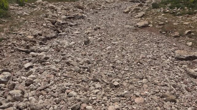 Dry riverbed winds through treeless mountains and barren hills across harsh arid valley floor. Parched channel eroded terrain suggest drought climate stress desertification under clear weather.