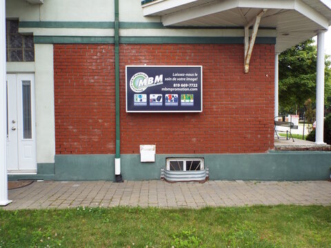 Gatineau, Quebec, Canada &ndash; July 02, 2026: A red brick building exterior features an "MBM Publicite Advertising" promotional sign mounted on the wall above a basement window on Boul. Saint-Ren&eacute; O.