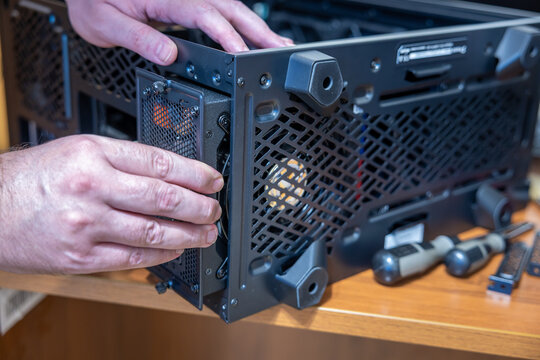A technician positions a power supply unit in the rear bay of a desktop computer case. The unit is lined up with the mounting holes before the screws go in. PC assembly or upgrade