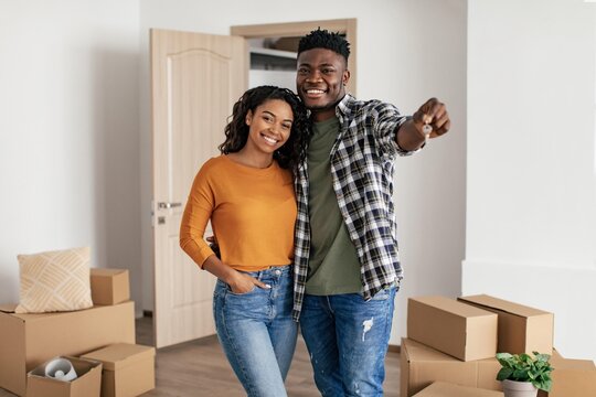 Smiling African American Couple In Their 20s Celebrating New Home Ownership While Unpacking Boxes In Living Room. They Are Happy And Enjoying This Exciting Moment Together In Their New Space.