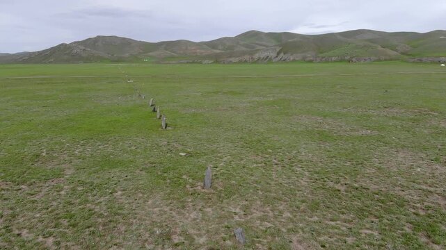 Ancient balbal stones align across Central Asian steppe as ancestral grave markers in Mongolia. Prehistoric memorial pillars suggest Turkic warrior heritage beside remote nomad burial ground.