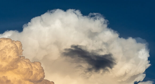 Contraste atmosf&eacute;rico: una peque&ntilde;a nube gris oscura flota frente a una gran formaci&oacute;n de c&uacute;mulos blancos bajo la brillante luz del sol.