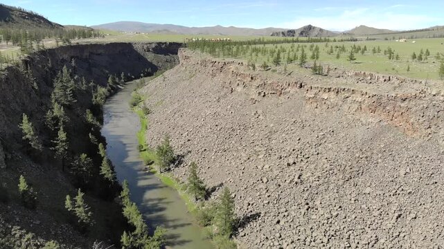 River carved rocky valley shaped by long term fluvial erosion seen from aerial drone view. Geomorphic landforms display sediment movement, ravine walls, watercut slopes, terrain evolution.