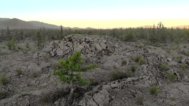 Basalt lava dome rises from cracked volcanic plain where trapped gas formed swollen rock. Frozen magma mound shows uplifted crust, barren igneous terrain, rugged geology.