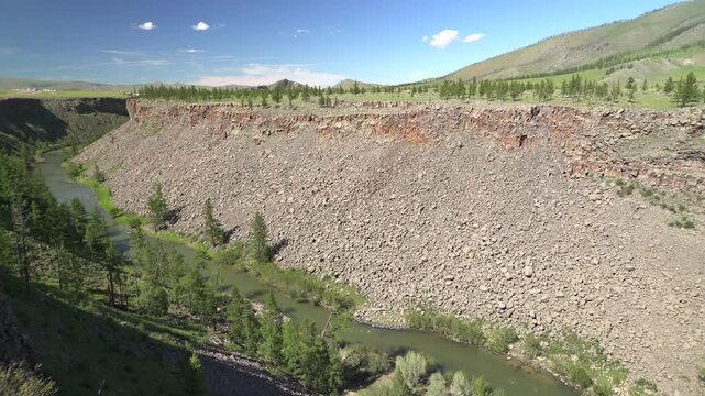 River flows along a deeply incised rocky valley shaped by long term fluvial erosion. Geomorphic landforms display sediment movement, ravine walls, watercut slopes, terrain evolution.