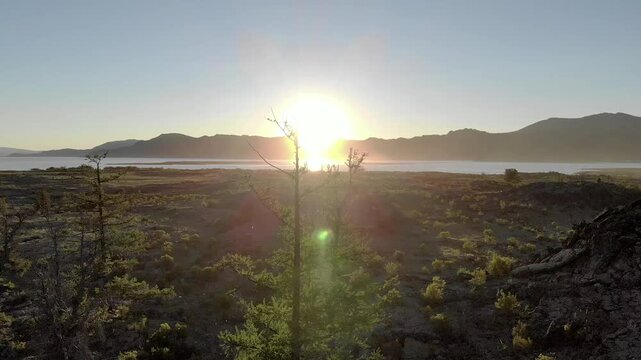 Sunrise drone view over a Central Asia lakeside basalt plain with lava rocks and volcanic terrain. Solidified magma meets quiet water, barren steppe, remote dawn atmosphere, earth science.
