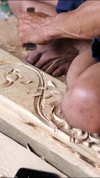 Wood carving artisan cuts ornamental pattern into soft wood with sharp chisel. Repeated hand pressure lifts thin chips, while carved border and floral motif grow clearer across each moment.