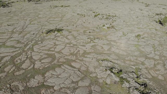 Drone aerial view shows frozen basalt lava plain with cracked rock textures plus badlands. Solidified magma forms igneous terrain across remote volcanic wilderness, barren relief.