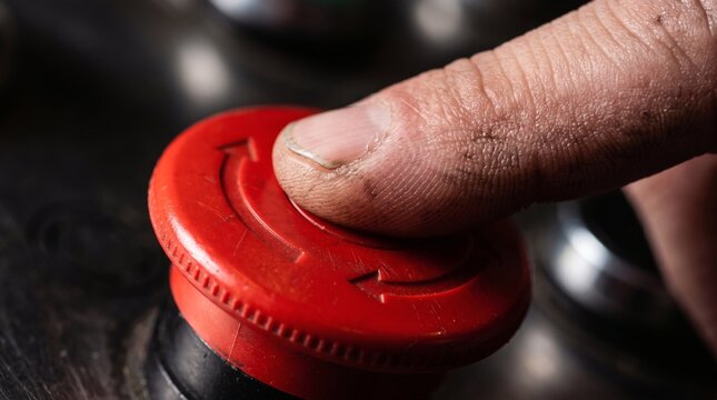 A close-up shot of a dirty finger pressing a red emergency stop button on industrial machinery.