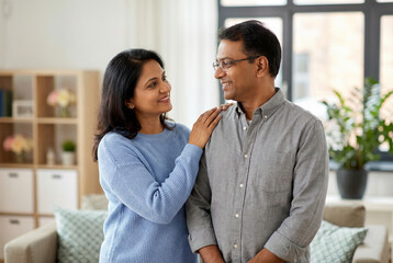 Obraz premium Happy Indian couple smiling at each other standing in modern living room with bright natural light at home