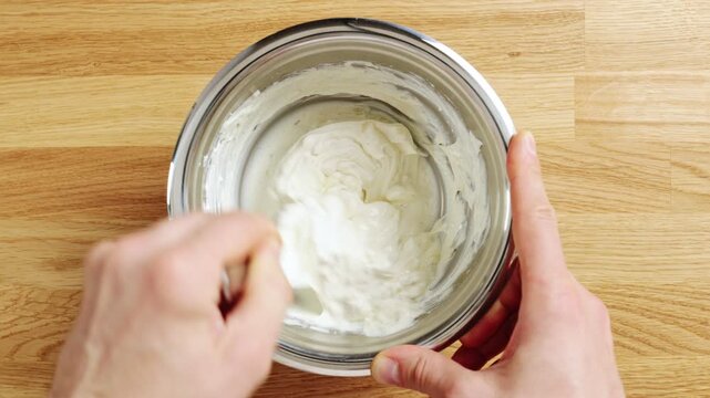Hand mixes whipped ricotta with Greek honey in bowl, timelapse. Creamy cheese adds protein to breakfast bowl with granola and nuts. Sweet spread pairs with berries, figs, seeds or seasonal fruit.