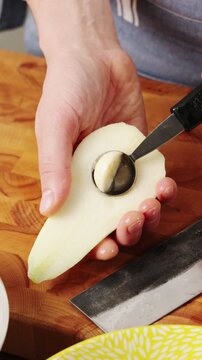 Melon baller removes core and seeds from pear half. Cooking lesson demonstrates safe grip and clean scooping technique. This fruit preparation works for poached pears, baked desserts, salads or tarts.