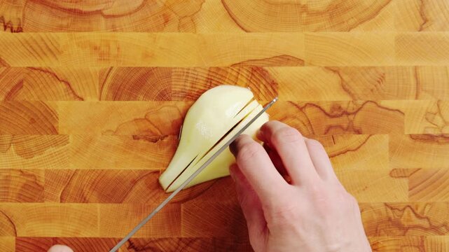 Knife cuts pear half into thin slices, close up. Fresh fruit makes sweet filling with cinnamon, butter and brown sugar. Chefs use sliced pears for rustic pie, French tart, galette or autumn dessert.