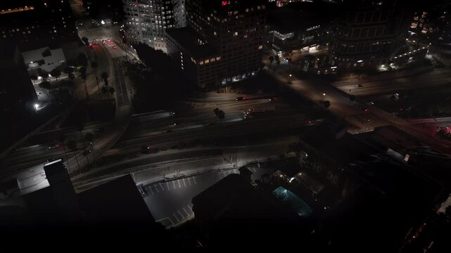 In downtown Los Angeles, California, cars and trucks are shown driving on the busy highway at night, viewed from an approaching aerial perspective.