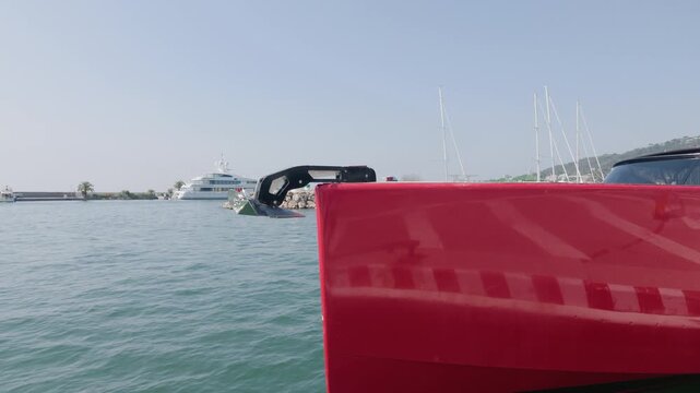 Close-up of a boat anchor and red hull near a stone breakwater with moored yachts, Cote d'Azur, France