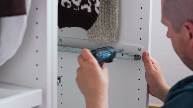 Person assembling white drawer unit using screwdriver, focusing on precise alignment of sliding mechanism in a well-lit indoor setting with neutral background elements