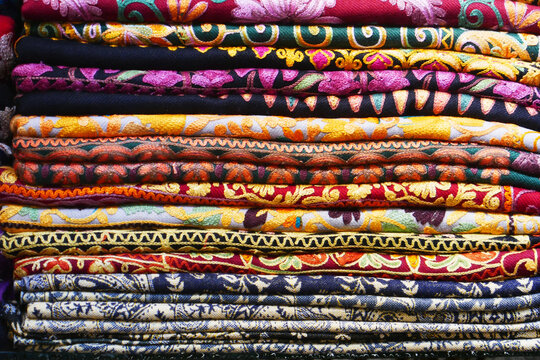 A colorful stack of folded embroidered textiles features rich patterns and vibrant hues.