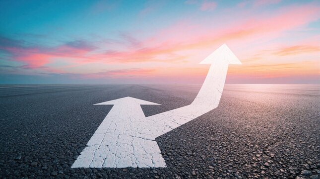 White arrows painted on asphalt road point toward horizon. One arrow splits and curves upward. Vast sky displays colorful sunset clouds. Represents growth and future direction.